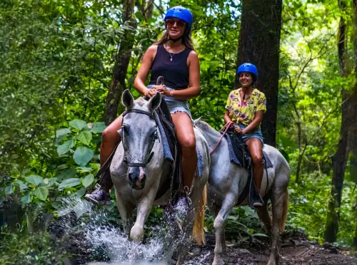 Two women riding horses through the rainforest jungle in Jaco